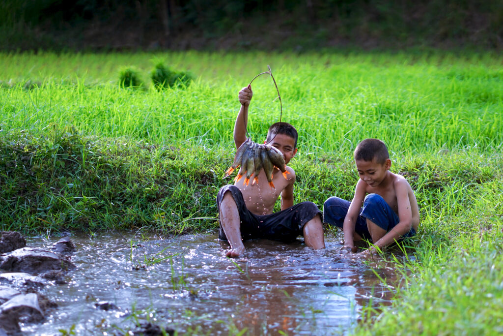 To børn fanger fisk i en dam i Thailand.